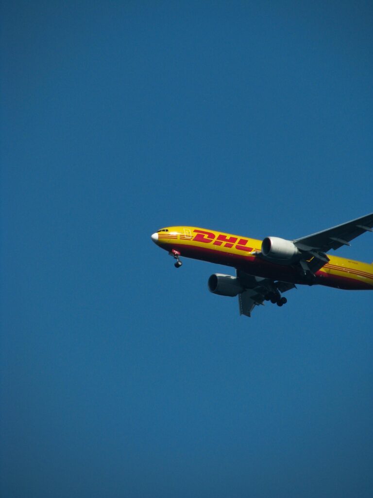 A DHL cargo plane flying against a clear blue sky during the day. Ideal for aviation and logistics themes.